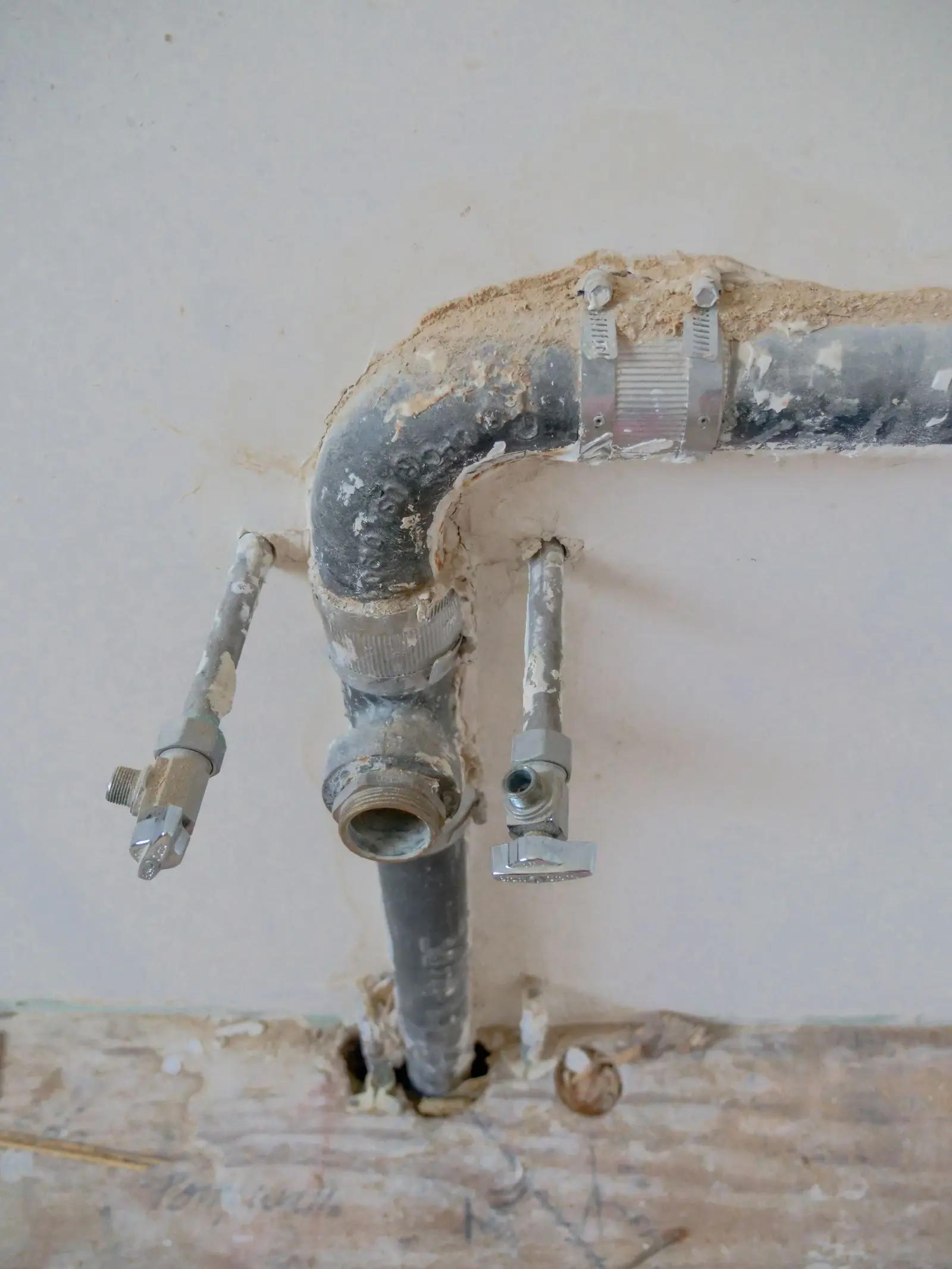 Old drain pipe and two water supply stop valves on an unfinished wall