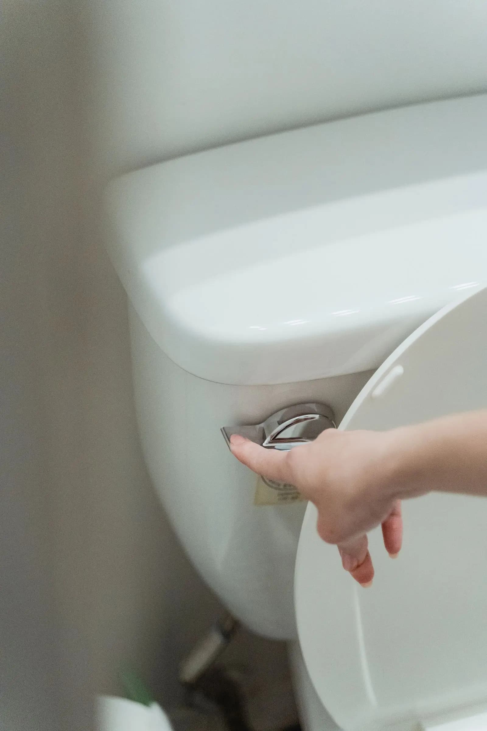 Hand pressing the flush lever on a toilet tank